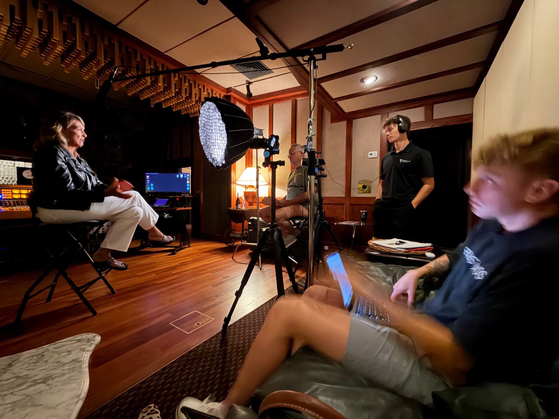 An on-camera interview being filmed in a recording studio control room, with lights, cameras and a boom microphone